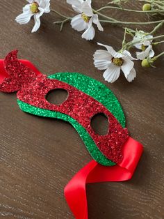 a red and green mask sitting on top of a wooden table next to white flowers