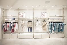 a clothing store with clothes on racks and hangings in the ceiling, all white