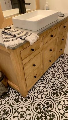 a white sink sitting on top of a wooden counter next to a mirror and tiled floor