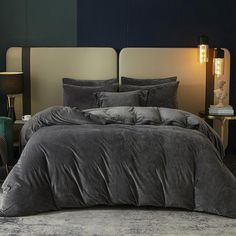 a bed with grey comforter and pillows in a dark room next to a lamp