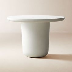 a white table with a round top on a plain surface in front of a light pink background