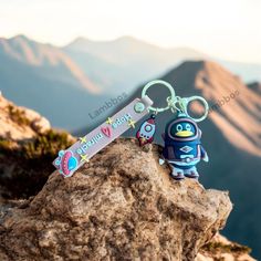 an animal keychain is sitting on top of a rock with mountains in the background