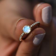 a woman's hand holding a ring with a white opal in the middle