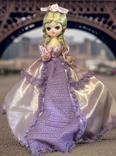 Introducing the exquisite 14-inch Korean Bradley doll from the 1970s, adorned in a magnificent purple satin gown that exudes elegance and grace. The gown features a huge hoop underneath, creating a dramatic poofy silhouette.  Adorned with purple lace trim at the bottom the dress also boasts a striking purple lace detail down the front. Her ensemble is completed with long puffy sleeves, adding to her regal appearance.  Perched atop her head is a purple satin bow, adorned with a large pink rose, a Vintage Victorian Satin Ball Gown, Vintage Satin Victorian Ball Gown, Vintage Satin Victorian Ball Gown Dress, Vintage Ruffled Ball Gown For Costume Party, Vintage Victorian Satin Costume Dress, Vintage Victorian Satin Dress For Costume, Vintage Satin Victorian Costume Dress, Vintage Satin Victorian Dress For Costume, Vintage Ball Gown With Attached Cancan