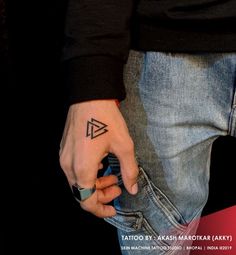 a person with a small triangle tattoo on their left hand, holding onto his jeans