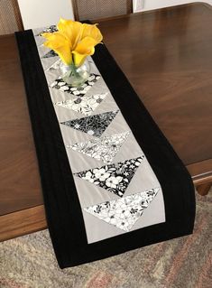 a vase with yellow flowers sitting on top of a wooden table next to a black and white runner