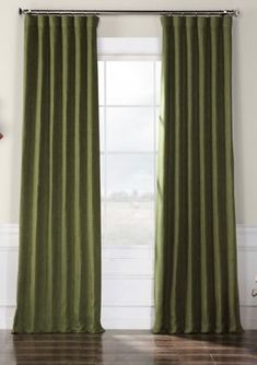 a green curtain hanging in front of a window with wood flooring and white walls