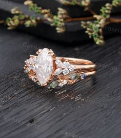 an engagement ring with two pear shaped diamonds and leaves on the side, sitting on a table