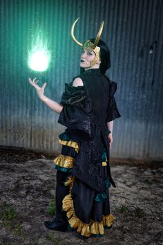 a woman dressed in black and gold holding a green ball with horns on her head