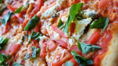 a close up view of a pizza with tomatoes and basil on it's crust