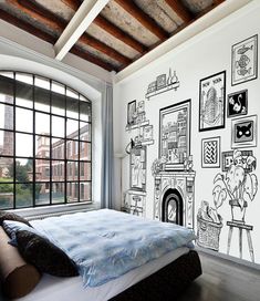 a bed sitting under a window next to a wall with pictures on it and windows