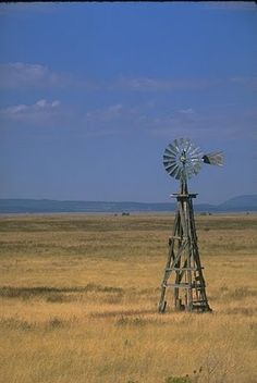 a windmill sitting in the middle of a dry grass field next to an open plain