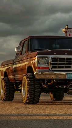 an old truck is parked on the side of the road in front of dark clouds