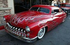 an old red car with flames painted on it's hood parked in front of a building