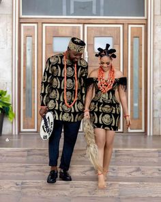 a man and woman dressed in african clothing walking down a hall way with an ostrich