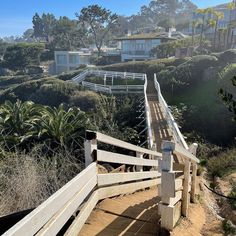 a wooden walkway leading to the beach with houses in the background and trees on both sides