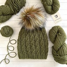 a green hat and two skeins of yarn on top of a white table