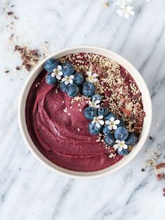 a close up of a bowl of food with berries and blueberries on it next to flowers