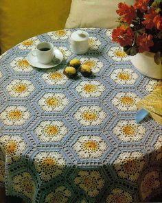 a crocheted table cloth with coffee cups on it next to a potted plant