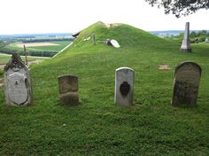 three headstones in the grass near a hill