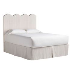 a white bed with an upholstered headboard and pleated bedskirt