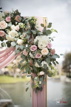 a wedding arch decorated with pink and white flowers, greenery and foliage for an outdoor ceremony