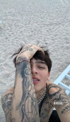 a man with tattoos sitting on the beach