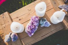 three white candles sitting on top of a wooden table next to rocks and crystals in the grass