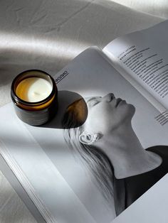 an open book with a jar of cream next to it on top of a table