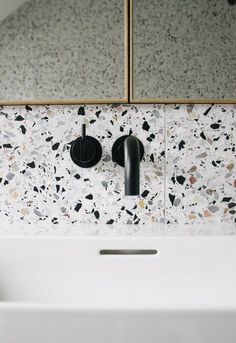 a bathroom sink with two black faucets on the wall and mirrors above it