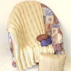 a crocheted blanket and pillow on a chair with knitting needles next to it