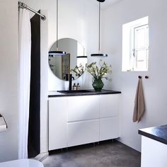 a white bathroom with black counter top and mirror above the sink, along with two vases filled with flowers