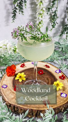 a cocktail with flowers in it sitting on top of a wooden slice that says woodland cocktail