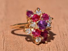 The Hempstead Bubblegum Ruby & Diamond Cocktail Ring. The ring features a reddish purple sapphire center stone with vivid red natural rubies and pink sapphires cascading from the center. Mixed between are diamonds throughout. The ring contains approximately 2 carats total weight by measurement of rubies and sapphires. The total estimated diamond weight by measurement is 0.36 carats. The ring is crafted in 14 karat yellow gold and is currently a finger size 6 yet can be adjusted to any finger Cluster Ruby Ring With Center Stone, Ruby Multi-stone Cluster Ring, Pink Ruby Rings With Multi-stone Detail, Red Ruby Multi-stone Ring With Diamonds, Red Ruby Diamond Multi-stone Ring, Red Multi-stone Sapphire Ring, Pink Ruby Diamond Ring With Multi-stones, Pink Diamond Cluster Ring With Multi-stone, Formal Multi-stone Pink Ruby Ring