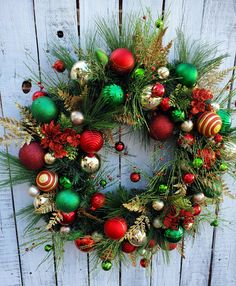 a christmas wreath with ornaments hanging on a wooden wall next to pine branches and other holiday decorations