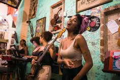 two women singing and playing guitars in a music room with other people sitting at tables