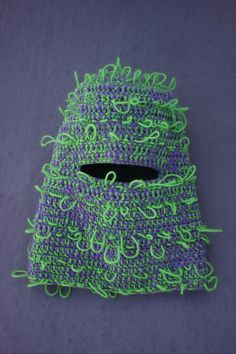 a green and purple crocheted object sitting on top of a gray table next to a black hole