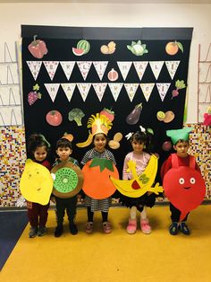 some kids are standing in front of a bulletin board with fruit and veggies on it