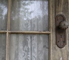 an old wooden door with a metal handle on the front and side glass doors that are covered in lace