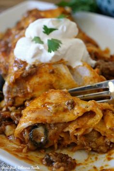 a white plate topped with lasagna covered in sauce and sour cream next to a fork