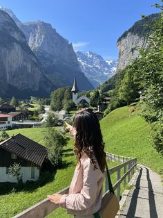 a woman standing on top of a wooden rail next to a lush green hillside covered in mountains