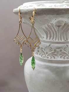 These vintage inspired earrings feature Art Deco style brass connectors and peridot green vintage glass beads. I love the intricate details and arabesque design of the brass connectors. They are lightweight yet sturdy, and extremely comfortable to wear. These long dangle earrings measure 2 1/2 inches long and hang from brass lever back ear wires. Perfect for a modern flapper look or a unique August birthday gift ABOUT THIS COLLECTION The sophisticated style of the Roaring Twenties is timeless. T Green Art Deco Drop Earrings, Vintage Green Brass Earrings, Vintage Gold Earrings For May Birthstone, Art Deco Green Jewelry For Pierced Ears, Elegant Green Brass Earrings, Green Metal Art Deco Jewelry, Victorian Green Dangle Earrings, Green Victorian Dangle Earrings, Elegant Green Chandelier Earrings In Brass