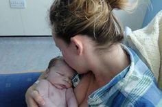 a woman holding a baby in her arms while sitting on a blue chair next to a wall