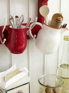 two red mugs with spoons hanging from them on a wall next to other kitchen utensils