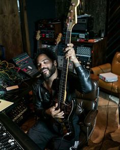 a man sitting in a chair with a guitar and sound equipment behind him, smiling at the camera