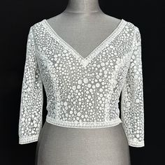 The Nina  3/4 sleeved lace bolero is a lovely Boho bridal top in an embroidered spotty foliage patterned lace. The ivory lace is finished with a linear crochet trim around the V neckline, cuffs and hem. The back is fastened with matching fabric-covered ivory buttons.  Hand-made in Edinburgh, using the finest lace and hand-sewn embellishments.  We use high quality bridal fabrics for our pieces - we portray the colour and textures of our bridal wear as accurately as possible through high-quality l V-neck Lace Top For Wedding, White V-neck Lace Top With Lace Sleeves, Wedding Top With Scalloped Lace And Long Sleeves, Lace Top With Long Sleeves For Wedding, Long Sleeve Lace Top For Wedding, Wedding Tops With Lace Sleeves, White Delicate Lace V-neck Top, White V-neck Lace Top With Delicate Lace, White V-neck Lace Top With Delicate Details