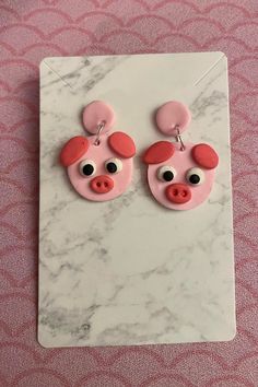 pink pig earrings with black eyes and ears on a marble slab, against a pink background