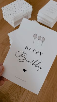 someone holding up a happy birthday card on top of a wooden table with other cards