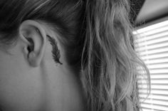 a woman's left ear has a feather tattoo on it