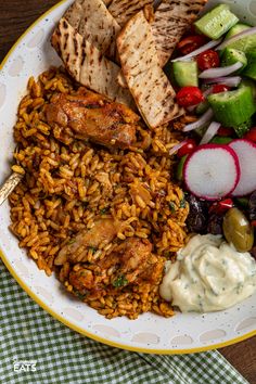 a white plate topped with lots of food next to veggies and pita bread